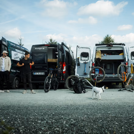 Bikes und Busse auf einem Schotterplatz am Wald